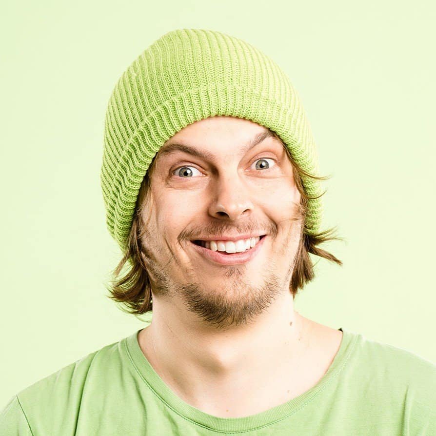 Smiling man with green beanie and shirt on light green background.