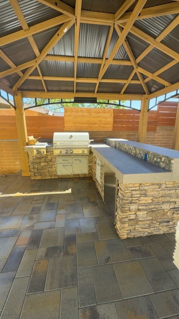 Custom outdoor kitchen with stone accents and bar seating by Precision Landworks.