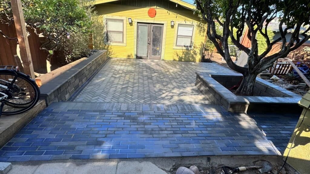Beautiful paved patio and landscaping with trees and a yellow building.