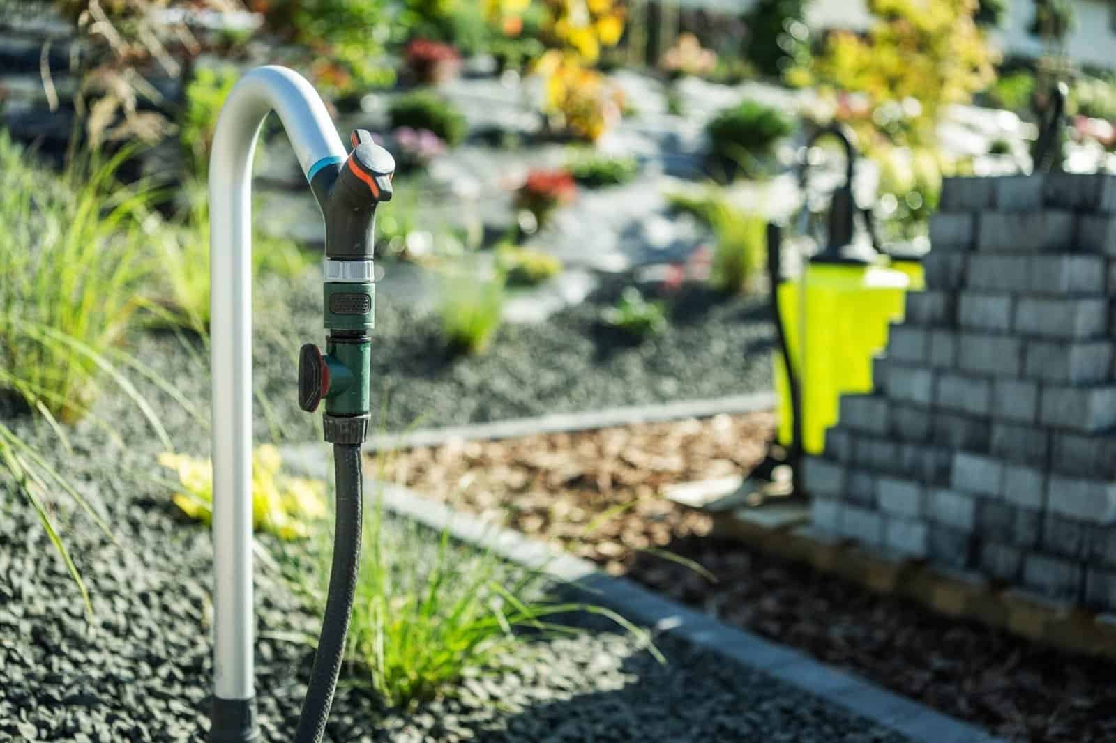 Garden irrigation system with hose and sprinkler in landscaped yard.