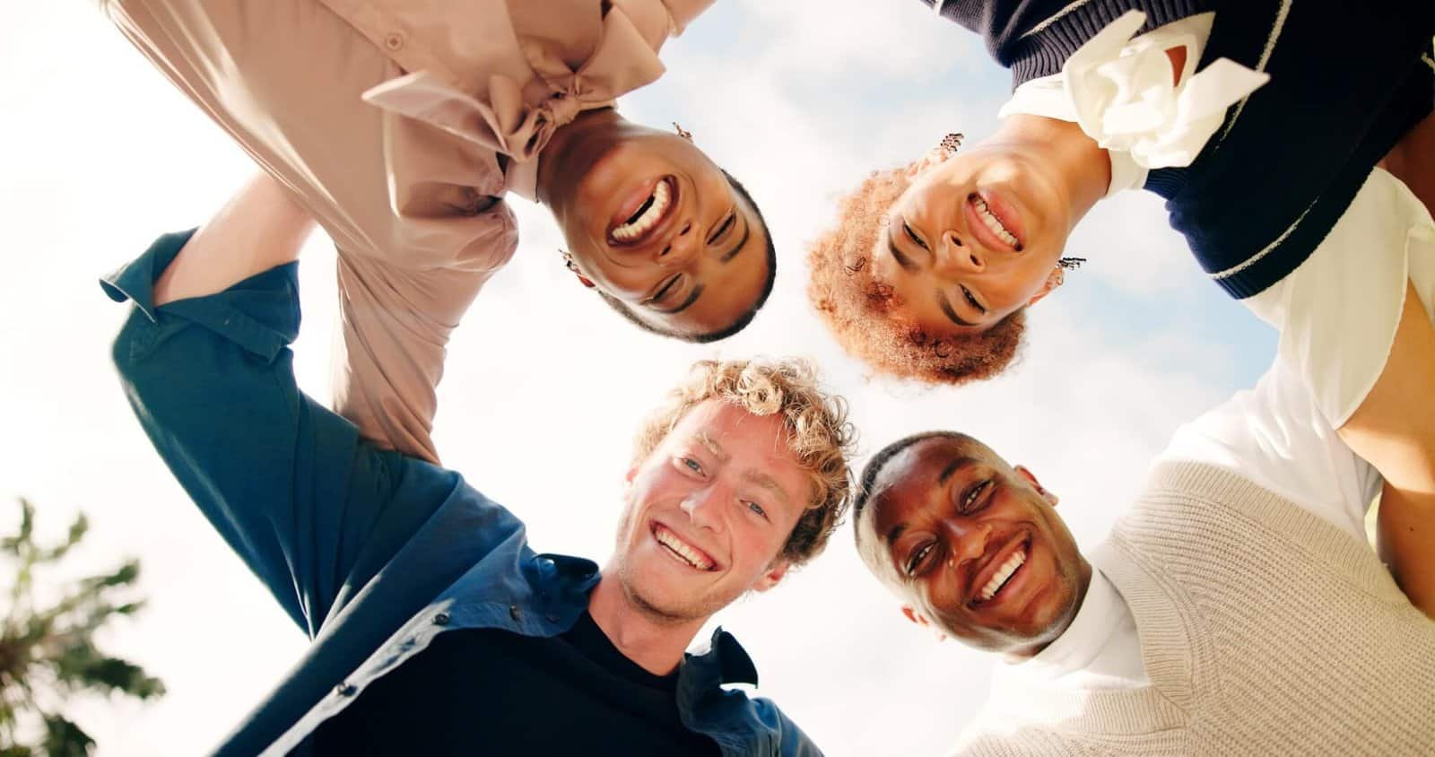 Diverse group of people smiling in a circle outdoors, representing teamwork and community.