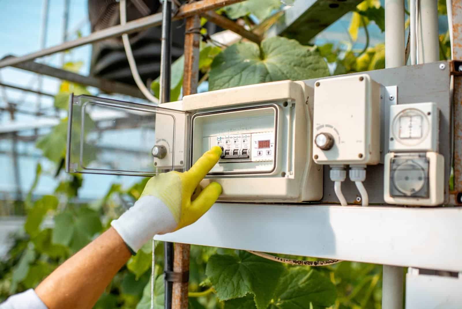 Person adjusting electrical control panel in greenhouse or farm setting.